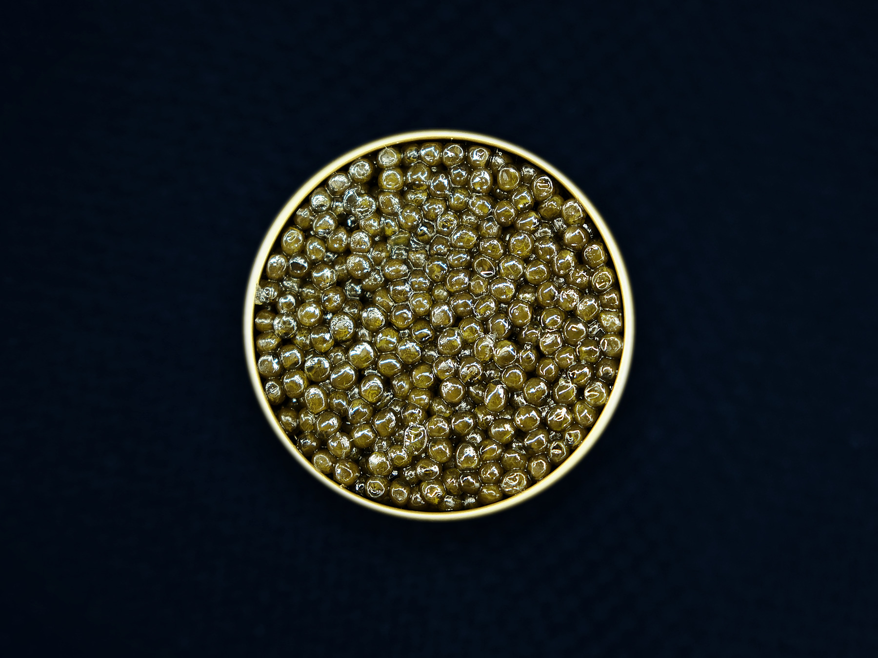 An open gold tin of AMANO caviar on midnight-blue textile — editorial presentation; natural batches vary