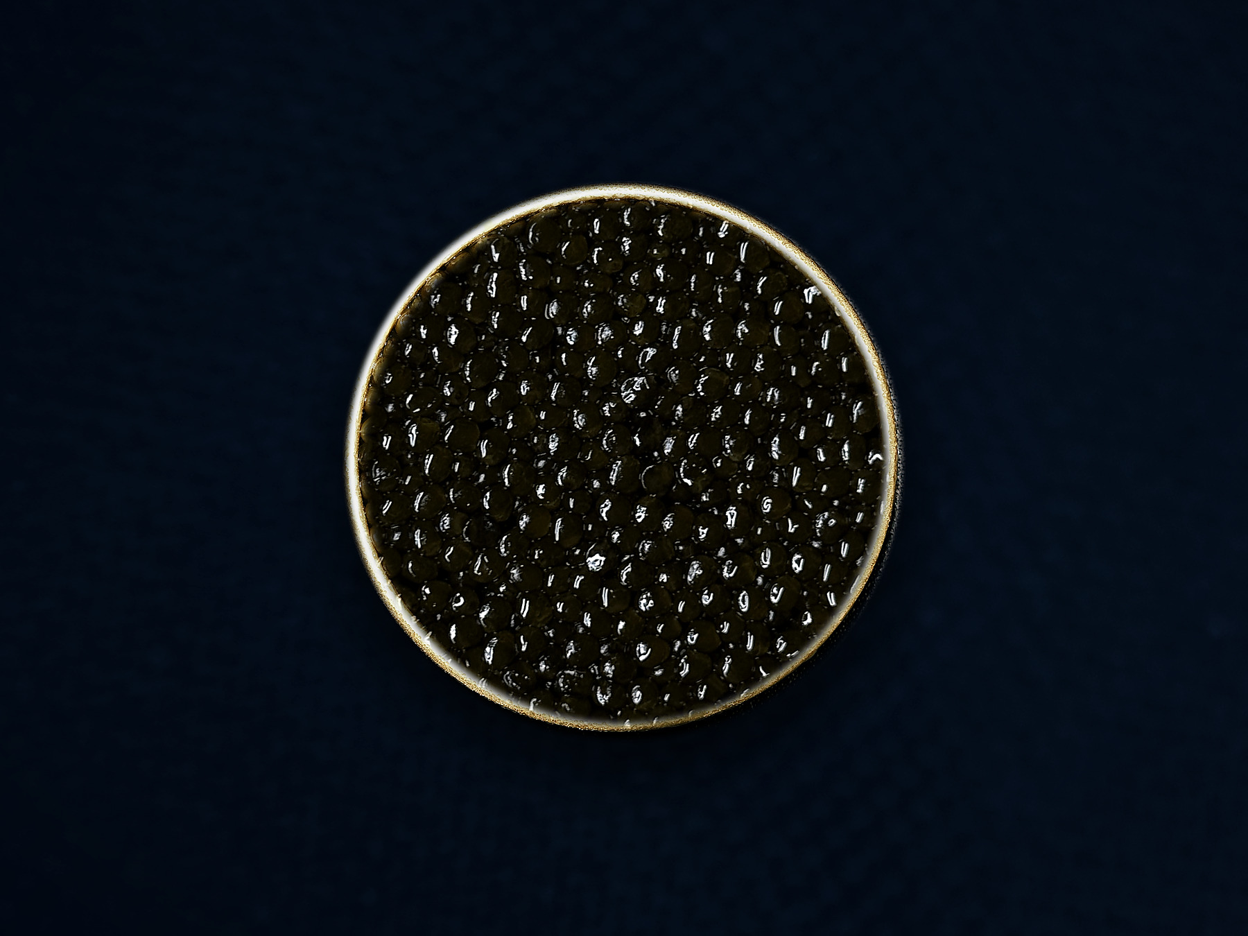 An open gold tin of AMANO caviar on midnight-blue textile — editorial presentation; natural batches vary